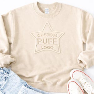 A beige sweater with a star-shaped logo, a pair of blue jeans, and a pair of white sneakers.