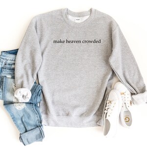 May include: Gray sweatshirt with the text "make heaven crowded" printed on the front. The sweatshirt is paired with blue jeans and white sneakers.