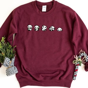K&ouml;nnte beinhalten: Burgunderfarbener Pullover mit einer Reihe von f&uuml;nf Pandas, die auf der Vorderseite aufgedruckt sind. Die Pandas sind alle nach vorne gerichtet und haben unterschiedliche Gesichtsausdr&uuml;cke.