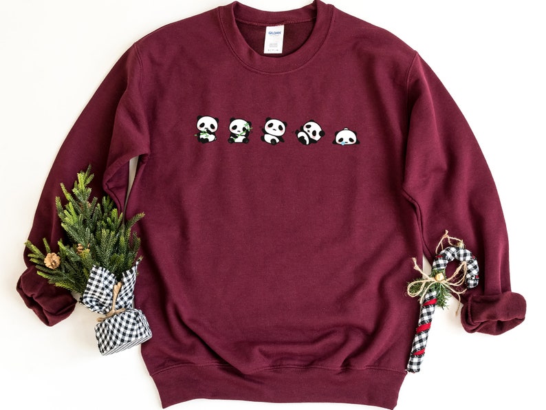 K&ouml;nnte beinhalten: Burgunderfarbener Pullover mit einer Reihe von f&uuml;nf Pandas, die auf der Vorderseite aufgedruckt sind. Die Pandas sind alle nach vorne gerichtet und haben unterschiedliche Gesichtsausdr&uuml;cke.