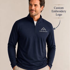 May include: A navy blue long-sleeve quarter-zip pullover featuring a white embroidered logo on the left chest that displays a mountain graphic above the text NORTHPOINT. The garment has a stand-up collar and a zipper closure at the neckline.