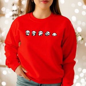 K&ouml;nnte beinhalten: Roter Pullover mit einem Aufdruck von f&uuml;nf Pandas, die Bambussprosse halten.