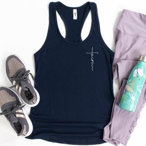 May include: A navy blue racerback tank top with the word faith written in white script forming a cross, paired with grey and rose gold athletic trainers, light purple leggings, and a teal water bottle with a white and pink floral pattern.