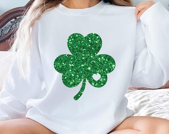 Könnte beinhalten: Weißer Pullover mit einem grünen Glitzer-Kleeblatt-Design. Das Kleeblatt hat ein kleines weißes Herz in der Mitte.