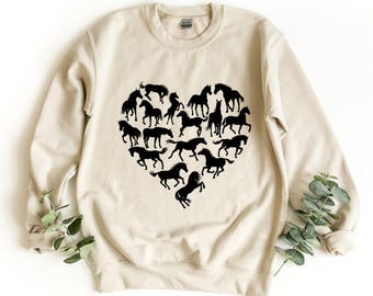 May include: A beige crewneck sweatshirt featuring a large graphic on the chest composed of multiple black horse silhouettes arranged in the shape of a heart. The long-sleeved garment has a ribbed collar, cuffs, and hem, with a standard fit.