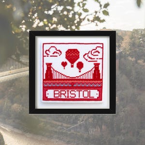Puede incluir: Un diseño de punto de cruz rojo y blanco del puente colgante de Clifton en Bristol, Inglaterra. El diseño incluye globos aerostáticos y la palabra "BRISTOL" en rojo.