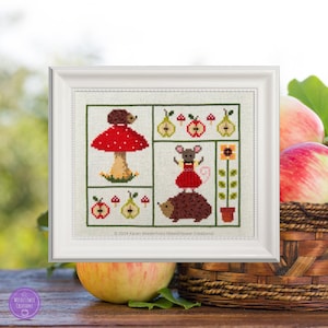 May include: A framed cross-stitch design featuring a red mushroom with a hedgehog on top, a mouse in a red dress, a hedgehog, and apples and pears. The design is surrounded by a white frame and the text "© 2024 Karen Wiederhold (Weedflower Creations)" is at the bottom.