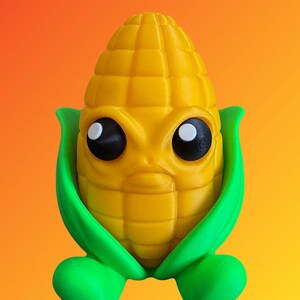 Op de afbeelding: Een geel, maïsvormig speelgoed met een lachend gezicht, grote zwarte ogen en groene bladeren en voeten. Het speelgoed staat tegen een oranje gradiënt achtergrond. Het speelgoed is een leuk, grillig ontwerp.