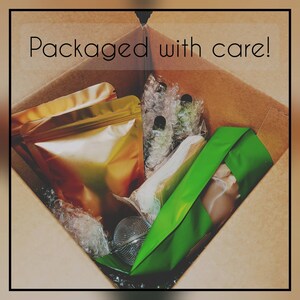 May include: A brown cardboard box containing various items, including gold and green pouches, clear bottles, and a tea infuser. The text "Packaged with care!" is displayed across the top of the box.