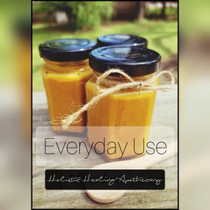 May include: Three glass jars filled with a golden yellow liquid, labeled "Everyday Use" and "Holistic Healing Apothecary". The jars are on a wooden surface with a wooden spoon.