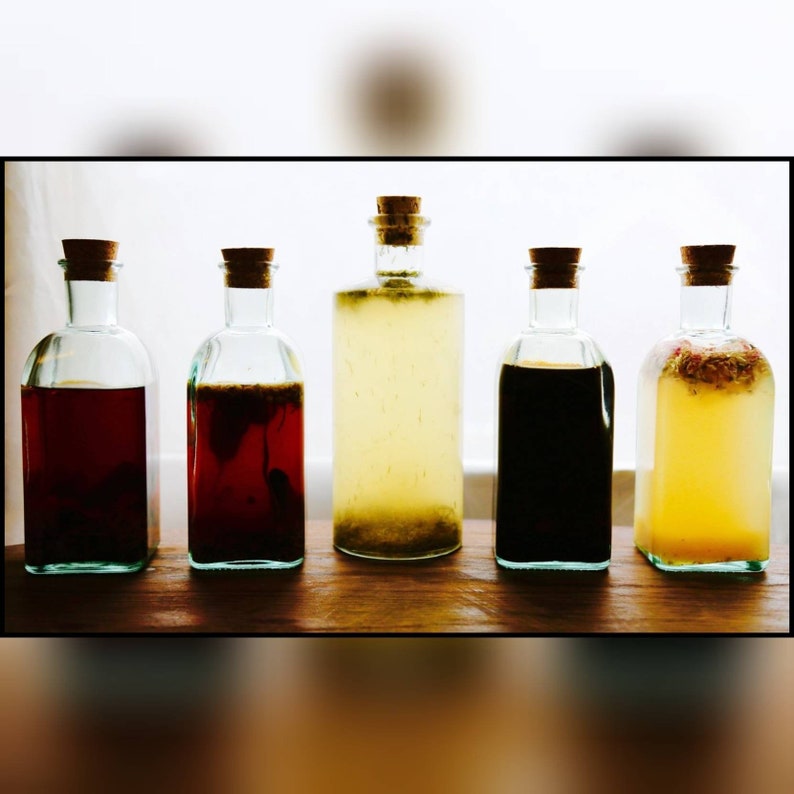 May include: Five glass bottles with cork stoppers, each filled with a different coloured liquid. The liquids vary from dark red to yellow, some with visible ingredients. The bottles are arranged on a wooden surface.