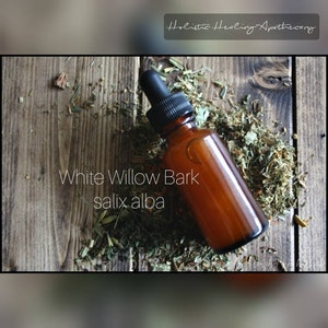 May include: A brown glass bottle with a dropper top, labeled "White Willow Bark salix alba". The bottle is sitting on a wooden surface with dried herbs.