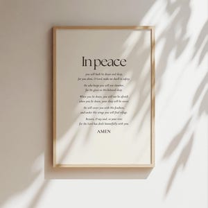 May include: A framed print featuring the words "In peace" and a poem in a dark brown font on a cream background. The frame is light brown wood. The print is displayed on a white wall. The text includes the word "sleepe".