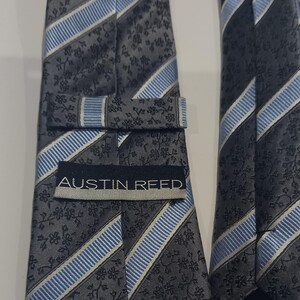 May include: A gray and blue striped tie with a floral pattern and the text "Austin Reed" on the front. The tie is made of 100% silk.