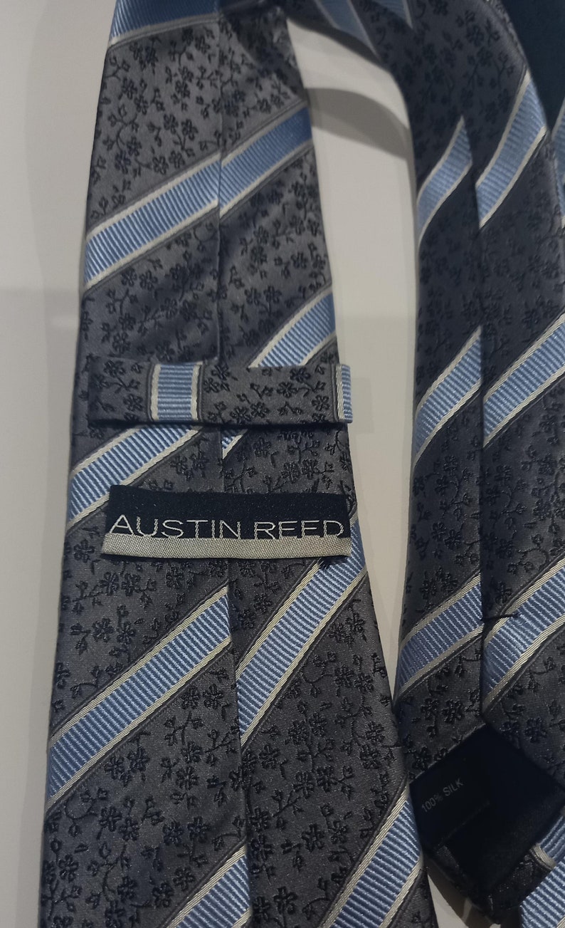 May include: A gray and blue striped tie with a floral pattern and the text "Austin Reed" on the front. The tie is made of 100% silk.