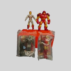 May include: Three Iron Man action figures in plastic packaging. The figures are red and gold, and one is silver. The figures are on a red and orange background.