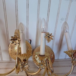 May include: A set of three gold-toned wall sconces with ornate details and clear glass bulbs. Each sconce has a curved arm and a decorative floral design.