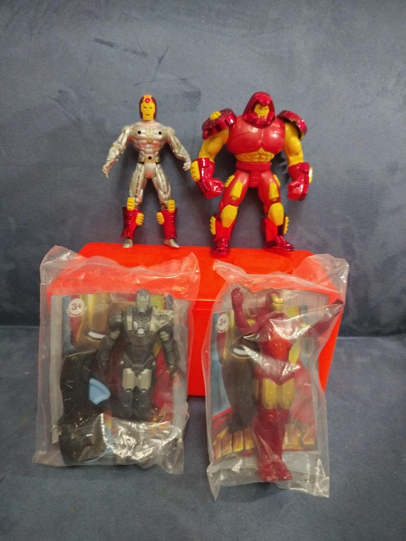 May include: Four Iron Man action figures in plastic packaging. The figures are red, silver, and black. The figures are from the Marvel Comics universe.