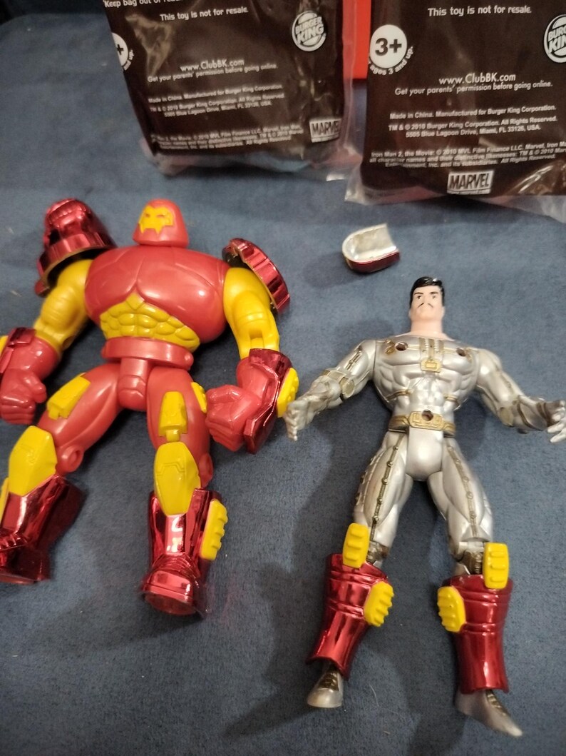 May include: Two action figures, one red and one silver, with yellow accents. The red figure is Iron Man, and the silver figure is a Marvel character. Both figures are posed in action stances.