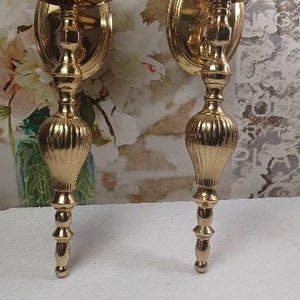 May include: A pair of gold metal wall sconces with a fluted design. Each sconce has a round base and a candle holder.