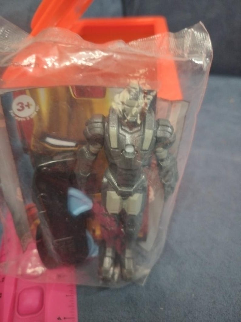 May include: A gray and silver action figure of Iron Man in a clear plastic bag with a red and gold cardboard box. The box has a 3+ age recommendation.