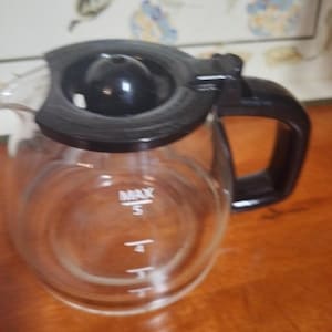 May include: A clear glass coffee pot with a black lid and handle. The pot has markings for 3, 4, and 5 cups. The maximum fill line is marked "MAX".