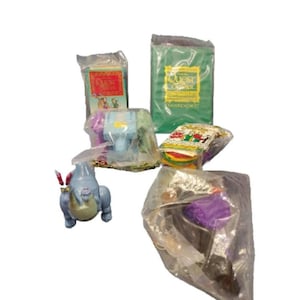 Puede incluir: Una colección de cinco bolsas de plástico selladas que contienen varios juguetes y juegos. Las bolsas contienen un dragón de juguete azul y morado, un castillo de juguete verde y azul, un libro verde con las palabras "Quest for the Crystal" en la portada, un libro multicolor con las palabras "The Adventures of..." en la portada, y un libro multicolor con las palabras "The Quest for the Crystal" en la portada.