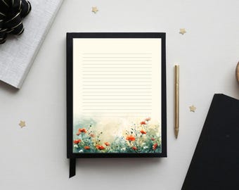 May include: A lined journal with a black cover and a watercolor floral design at the bottom. The design features red poppies and green foliage. A gold pen rests beside the journal.