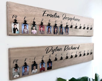 May include: Two rectangular light wood boards mounted on a wall, each featuring the name Emelia Josephine or Dylan Richard in black script. Each board has black metal clips labeled PK, K, and 1 through 12, holding small school portrait photos.