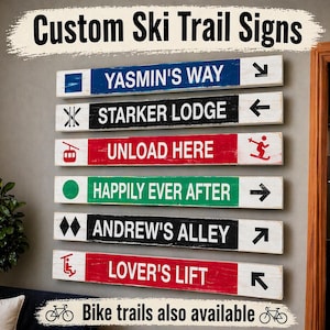 May include: A collection of custom ski trail signs with various names and directional arrows. The signs are rectangular, with a distressed wood appearance and colorful backgrounds. Text includes "YASMIN'S WAY," "STARKER LODGE," "UNLOAD HERE," "HAPPILY EVER AFTER," "ANDREW'S ALLEY," and "LOVER'S LIFT." Bike trails are also available.
