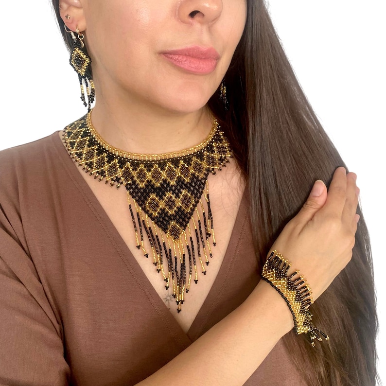 May include: A beaded jewelry set featuring a necklace, bracelet, and earrings. The set has a black and gold geometric pattern. The necklace has a bib-style design with dangling beads. The bracelet and earrings match the necklace.