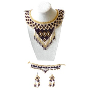 May include: A beaded jewelry set featuring a statement necklace, bracelet, and earrings. The necklace is displayed on a white bust, showcasing a geometric pattern in gold, white, and dark purple beads. The bracelet and earrings mirror the necklace's design.
