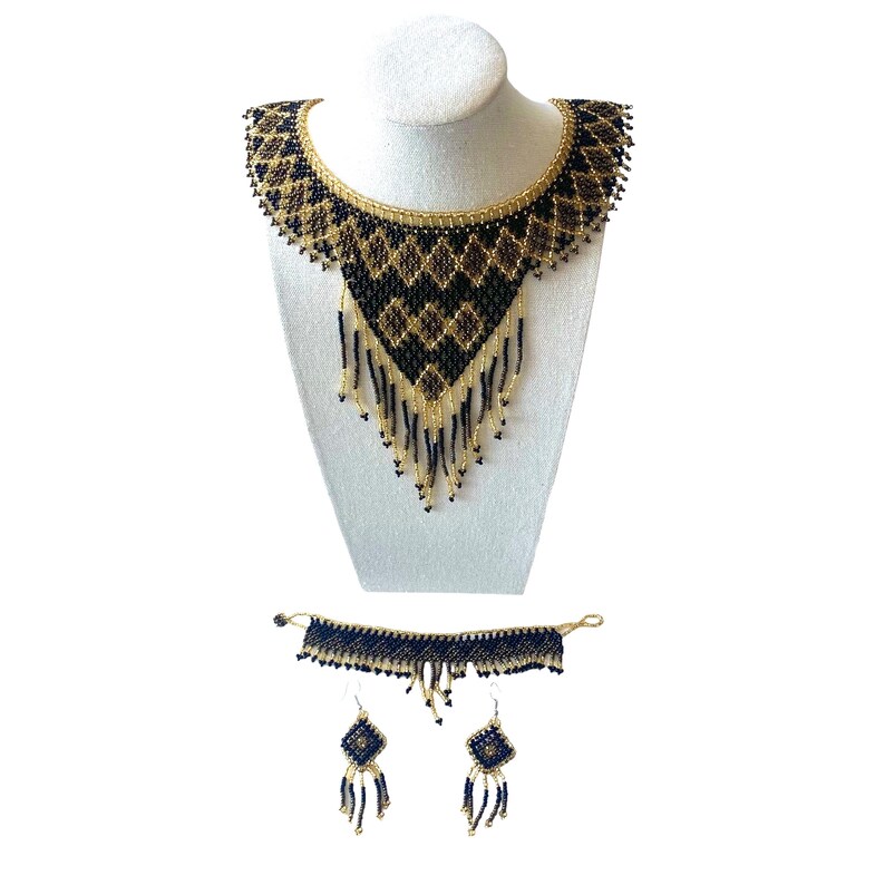 May include: A beaded jewelry set featuring a statement necklace, bracelet, and earrings. The necklace is displayed on a white mannequin bust. The set features black and gold beads in a geometric pattern with fringe.
