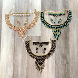 May include: Three beaded jewelry sets, each including a necklace, bracelet, and earrings. The sets feature intricate patterns in gold, black, and turquoise, and gold, white, and pink. The necklaces have a bib design with dangling fringe.
