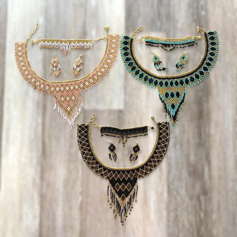 May include: Three beaded jewelry sets, each including a necklace, bracelet, and earrings. The sets feature intricate patterns in gold, black, and turquoise, and gold, white, and pink. The necklaces have a bib design with dangling fringe.