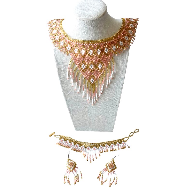 May include: A beaded jewelry set featuring a necklace, bracelet, and earrings. The necklace is displayed on a mannequin and has a pink, gold, and white geometric design. The bracelet and earrings mirror the necklace's design.