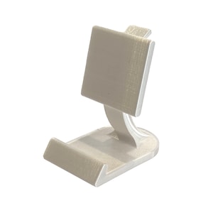 May include: A white 3D printed phone stand with a square top and a curved base.