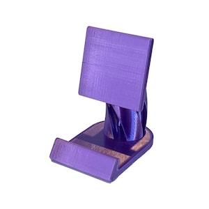 Puede incluir: Un soporte para teléfono de color morado impreso en 3D con una base retorcida y una parte superior plana para sostener un teléfono.