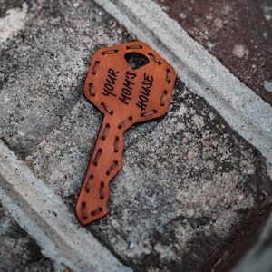 May include: A brown leather key shaped keychain with the text "YOUR MOM'S HOUSE" engraved on it.