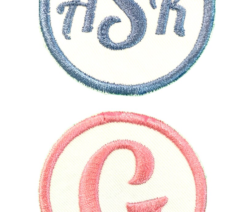 K&ouml;nnte beinhalten: Zwei gestickte Aufn&auml;her, einer mit einem blauen "Sh" in einem wei&szlig;en Kreis mit einem blauen Rand, und der andere mit einem rosa "C" in einem wei&szlig;en Kreis mit einem rosa Rand.