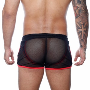 May include: Black mesh shorts with red trim and accents. The shorts have a drawstring waistband and a sporty design. The see-through fabric reveals the wearer's skin. The shorts are designed for athletic activities or casual wear.