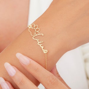 May include: Gold bracelet with a paw print charm and the name "Valina" written in cursive.