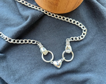 May include: A silver chain necklace with two hand-shaped charms and a heart pendant.