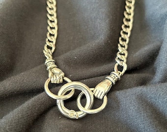 May include: A silver chain necklace with a unique clasp featuring two interlocking rings and two hand-shaped designs.