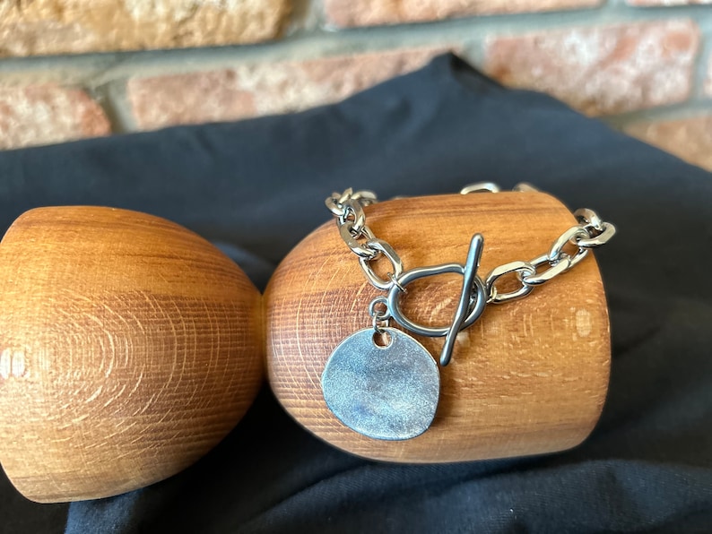 May include: A silver chain bracelet with a large, round, silver charm. The bracelet has a toggle clasp.