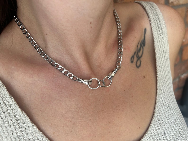May include: A silver chain necklace with two silver hand-shaped clasps and a silver ring connecting them.