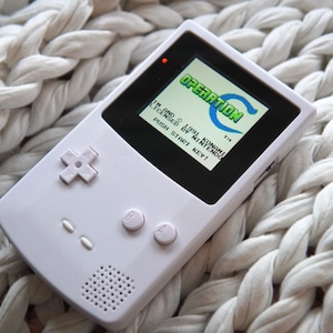 May include: A white handheld game console with a black screen displaying the text "OPERATION" and "TM" and the text "1991 KONAMI LICENSED BY NINTENDO" and "PUSH START KEY!" in green and white text.