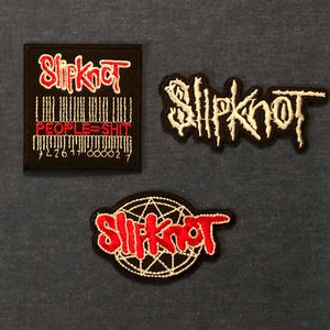 May include: Three embroidered patches featuring the band name "Slipknot" in red and white. One patch includes the text "PEOPLE=SHIT" below a barcode design. The patches are black with white or red stitching.