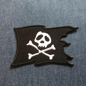 May include: Black pirate flag patch with a white skull and crossbones design. The flag has a tattered edge, giving it a vintage look. This patch is ideal for jackets, bags, or other fabric items.