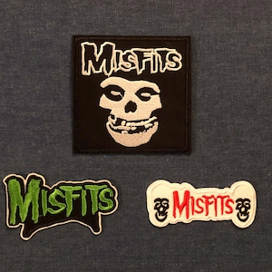 May include: Three embroidered patches featuring the band "Misfits". The top patch is square, black with a white skull and the word "Misfits". The other two patches have the word "Misfits" in green and red, respectively, with skull imagery.
